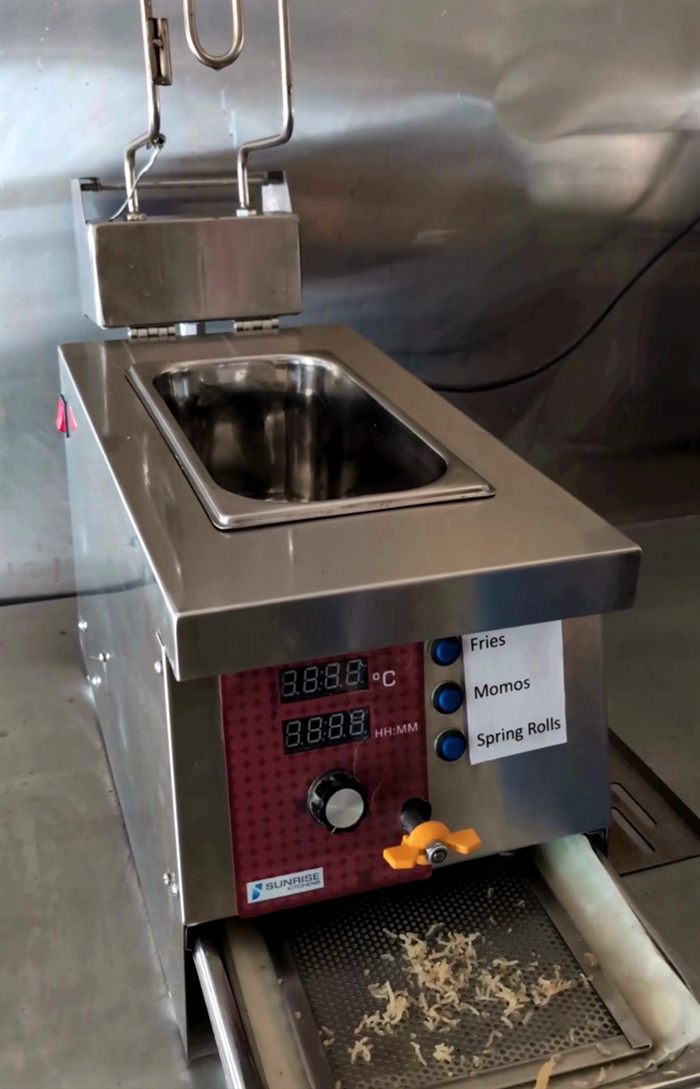 Total Fryer with the oil filtration drawer pulled out, showing food debris caught on the perforated filter screen